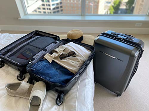 Open suitcase on bed with clothes and travel items, next to a closed suitcase.